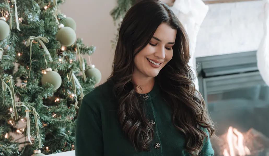 Pastora Mowana Débora sentada, sorrindo, ao lado de uma árvore de Natal